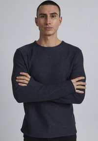 Navyblaues, gestricktes Langarmshirt mit strukturiertem Finish, Rundhalsausschnitt und leicht lockerer Passform. Verfügt über verlängerte Bündchen für zusätzlichen Komfort.