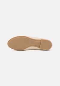 Scarpa beige con tomaia liscia, punta arrotondata e suola in gomma texturizzata. La suola presenta un tacco leggero e scanalature orizzontali per una maggiore aderenza.
