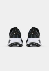 Een paar zwart-witte Nike hardloopschoenen gezien van achteren, met dikke, gewatteerde zolen en reflecterende stripes.