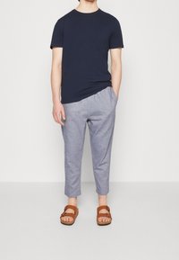 Námořnicky modré bavlněné tričko v kombinaci s lehce šedými lněnými kalhotami a hnědými sandály. Kalhoty mají volný střih a boční kapsy.