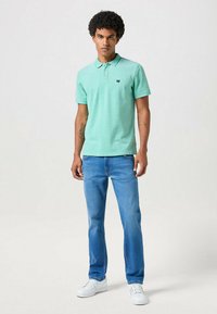 Polo verde menta con colletto, abbinato a jeans azzurri. Sneakers bianche completano l'outfit, presentando un semplice dettaglio del logo.