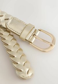 Kuldne puuvillane nahkvöö, millel on sile ja läikiv pind ning metallist sulg, millel on poleeritud viimistlus. Lähedalt vaatamine kinnitusele.