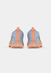 Un par de zapatillas de correr de color azul claro con suelas naranjas y tiradores verticales naranjas en el talón, visto desde atrás sobre un fondo blanco.