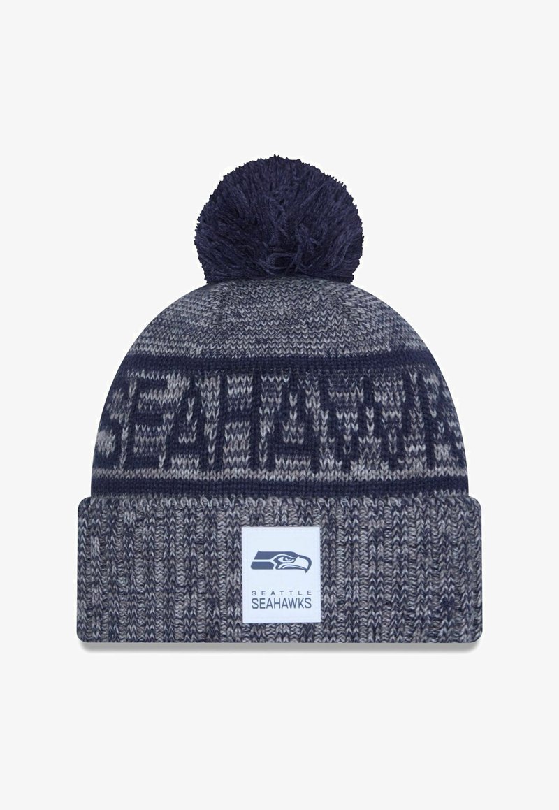 Knitted beanie in navy and gray with a pom-pom on top. Features a “Seattle Seahawks” logo patch and textured patterns.