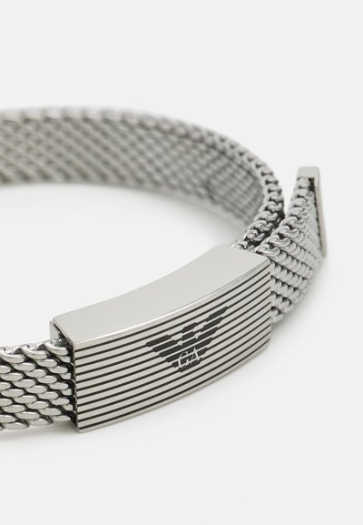 Bracciale in rete metallica con chiusura rettangolare argento caratterizzata da strisce orizzontali e un logo. Texture elegante e liscia con un finish lucido.