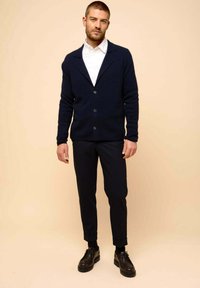 Marinblå ullkofta med sjalkrage, knappstängning och texturerad tyg, kombinerad med slim-fit svarta byxor och svarta skor.