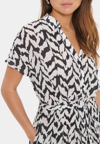 Sukienka w czarno-białe wzory, wykonana z teksturowanej tkaniny, z krótkimi rękawami, kołnierzykiem i wiązanym detalem w talii.