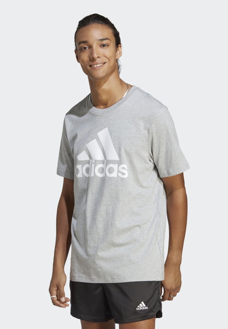Pelēka T-kreklu ar īsām piedurknēm un lielu baltu Adidas logo priekšpusē, izgatavots no mīksta auduma. Saskaņots ar melniem šortiem ar mazu logo.