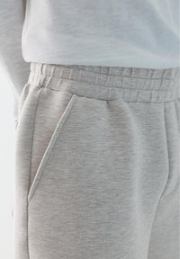 Gros plan d'une personne portant un pantalon de jogging gris clair avec une taille élastique et une poche latérale, associé à un haut blanc.