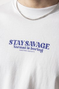 Biele bavlnené tričko s fialovým grafickým potlačou, na ktorom je text "STAY SAVAGE Normal is boring" a pod ním "KAOTIKO SOCIETY".