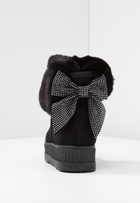 Svart mocka ankelstövel med en plyschfoder och en stor svart rosett prydd med silverstrass på baksidan. Plattformssula.