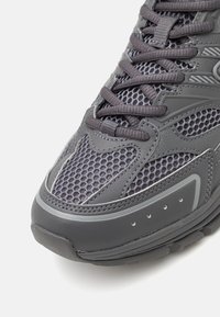 Šedá sportovní obuv kombinující prodyšnou síťovinu a syntetickou kůži. Výrazná gumová podrážka s vzorovaným vzorkem pro lepší přilnavost.