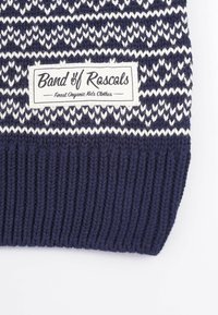 Stickad marinblå mössa med ribbad textur, prydd med ett vitt geometriskt mönster och en logotypetikett för "Band of Rascals" framtill.