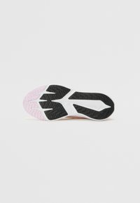 Suela de zapatilla deportiva de goma con un patrón de tracción ondulado en negro, media suela blanca y detalles en rosa claro. Textura suave con agarre estructurado.