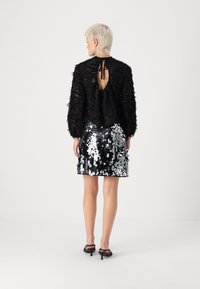 Μαύρη μπλούζα με υφή, μακριά μανίκια και σχέδιο κλειδαρότρυπας στο πίσω μέρος. Συνδυασμένη με μίνι φούστα με �ασημί παγιέτες. Ορατά μαύρα τακούνια.