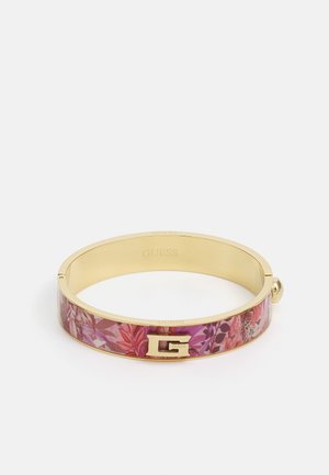Bracelet jonc couleur or avec motif floral rose et un emblème "G" doré sur le devant, marqué "GUESS" à l'intérieur.
