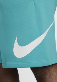 Pantalones cortos deportivos turquesa hechos de una tela texturizada, con un gran logo de Nike en color blanco en el lado y una cinturilla normal.