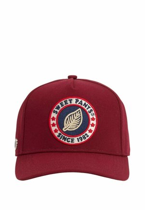 Casquette de baseball marron avec un patch rond montrant une feuille à l'intérieur d'un cercle bleu, texte "Sweet Pants Since 1982" et des étoiles rouges autour de la bordure.