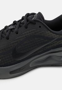 Musta Nike-juoksukenkä, jossa on verkkomateriaali, mustat nauhat ja paksu, pehmustettu pohja valkoista taustaa vasten.