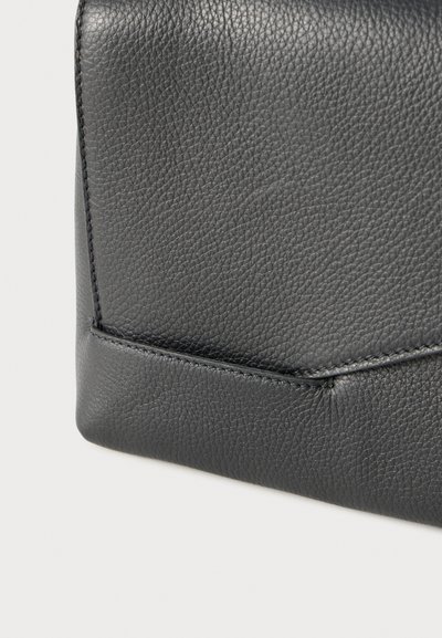 Prim-plan cu colț de piele neagră texturată, cu cusături detaliate pe un accesoriu din piele, pe un fundal deschis.