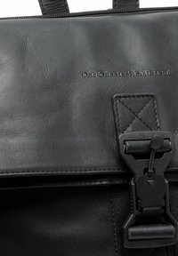 Zwarte leren laptoptas met een gestructureerde afwerking, gestikte accenten en een Fidlock magnetische sluiting. Merkaanduiding in reliëf op de voorkant.