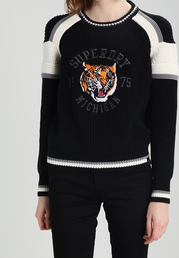 Pull en maille noir avec des rayures blanches sur les épaules et les poignets, arborant un tigre rugissant et le texte "Superdry Michigan 1975" sur le devant.