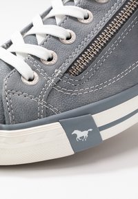 Sneaker grigio texturizzato con lacci bianchi, zip argentata come dettaglio, e una suola in gomma bianca con una striscia blu e il logo di un cavallo sul tallone.