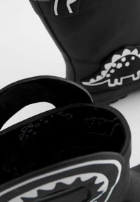 Bottes en caoutchouc noires avec un design de dinosaure en blanc. Possèdent une surface texturée, une forme arrondie et un haut ouvert pour un enfilage facile.