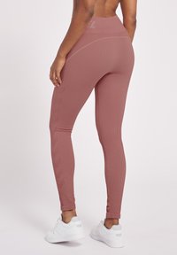 Ribbstickade rosa leggings med hög midja och sidologotillbehör. Tillverkade av stretchigt tyg, den åtsittande designen förbättrar rörligheten, kombinerat med vita sneakers.
