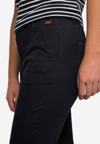 Pantaloni scuri blu notte dal taglio slim, con cuciture arancioni e un logo ricamato decorativo in vita. Texture liscia e tasche funzionali.