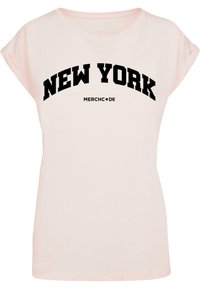 Heledad roosa puuvillane T-särk, millel on volditud varrukad. Esiküljel on julge musta värvi tekst, mis ütleb "NEW YORK" sõna "MERCHC•DE" kohal. Klassikaline ümar kaeluse disain.