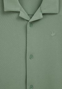 Hellgrünes, strukturiertes Polohemd mit kurzen Ärmeln, einem umgeschlagenen Kragen, einer Knopfleiste mit drei Knöpfen und einem kleinen, auf der Brust aufgestickten Vogel-Logo.