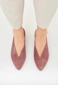 Pantofi slip-on din suede în nuanță de mauve, cu vârf ascuțit și decolteu mic. Prezintă cusături contrastante pe margine. Textură netedă.