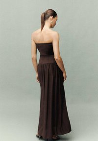 Maxi dress marrone senza spalline con un corsetto aderente e una gonna fluida, realizzato in tessuto morbido. Design semplice con una texture liscia.