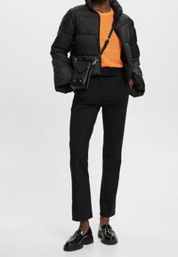 Svart pufferjacka med en kort design, orange stickad tröja, svarta skräddarsydda byxor och blanka svarta loafers. Liten svart axelväska.