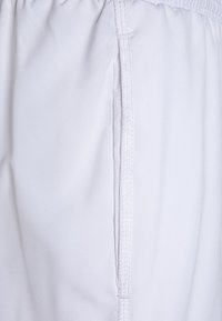 Primer plano de pantalones con cintura elástica blanca, con costura lateral visible y una sutil textura de la tela.