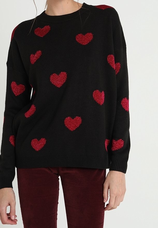 Musta neulepaita, jossa löysä istuvuus ja punaisilla kimaltavilla sydänkuvioilla koristeltu, resorit hihoissa ja helmassa. Yhdistetty viininpunaisiin housuihin.