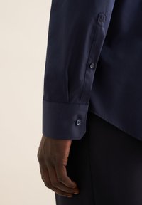 Marineblauwe blouse met lange mouwen, weergegeven met de nadruk op de manchetten, met knoopdetails en een gladde stofstructuur.