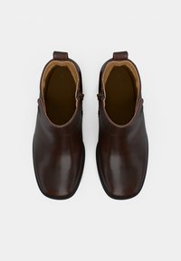 Par de botas de tornozelo de couro castanho escuro, tipo slip-on, com fechos laterais e forro interior bege, vista de cima sobre um fundo branco.