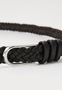 Musta nahkavyö, jossa on kudottu pinta, varustettuna hopeanvärisellä metallisoljella ja kolmella mustalla nahkalenkillä. "MICHAEL KORS" -logo on kohokuvioitu solkeen.
