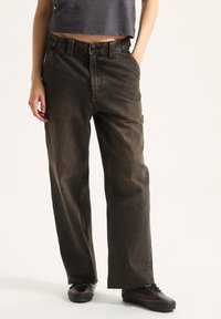 Pantalones de mezclilla oscuros, holgados y de talle alto, con cierre de botón, presillas para cinturón y bolsillos delanteros; detalle de dobladillo deshilachado.