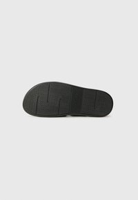 Black rubber shoe sole with a zigzag tread pattern. Features a textured surface and logo in the middle, designed for traction and durability.