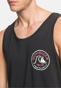 Canottiera nera in cotone con un logo circolare bianco e rosa con la scritta "Quiksilver" e "1969", progettata per il comfort e l'abbigliamento casual.