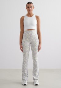 Hoge taille bloemenleggings van licht materiaal met een pastelkleurig patroon; gecombineerd met een witte cropped sporttop en witte sneakers.