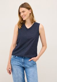Granatowy top bez rękawów z dekoltem w serek, z teksturowanym wzorem w paski. Połączony z jasnoniebieskimi dżinsami.