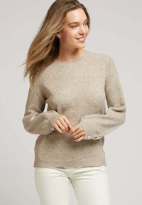 Pull en tricot beige avec de longues manches bouffantes et un ourlet côtelé. Design à col rond et détails de boutons subtils au niveau des poignets.