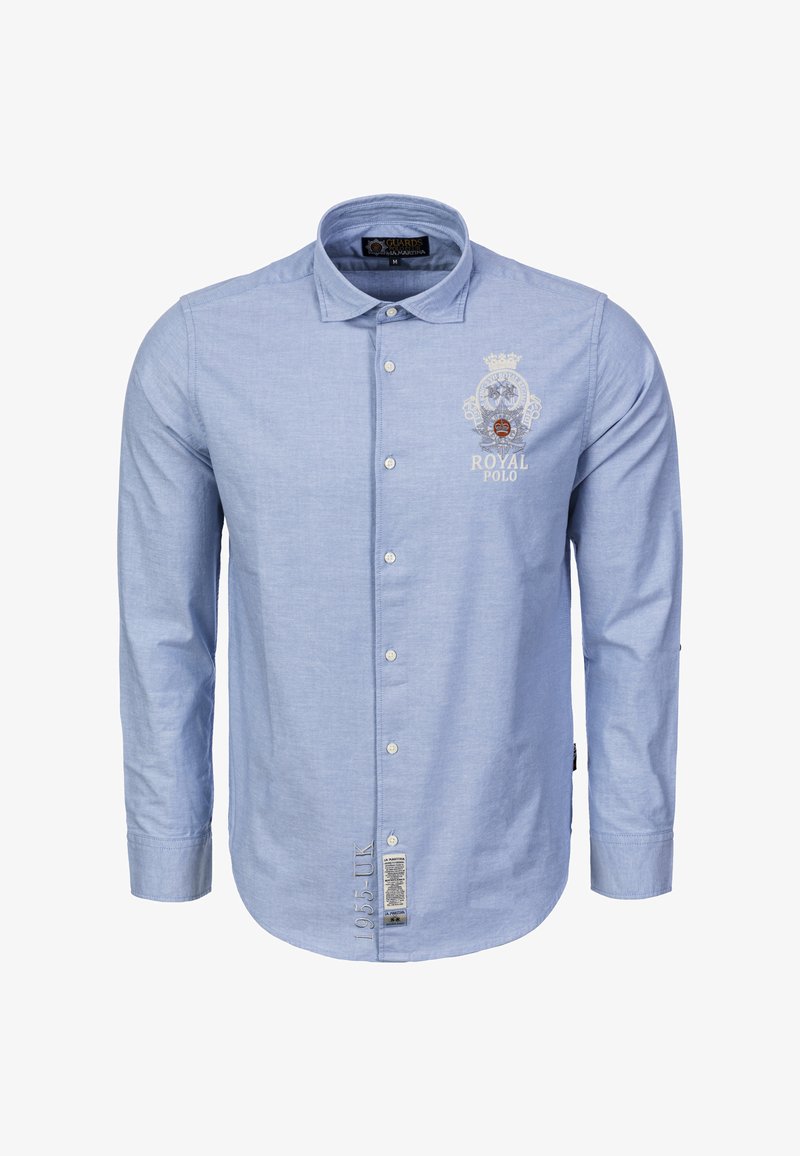 Chemise à manches longues bleu clair avec un col boutonné, un logo brodé sur la poitrine et des coutures détaillées près de l'ourlet.
