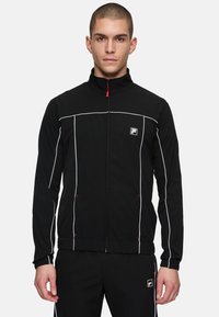 Zwarte zip-up jas met witte accentlijnen en logo op de linkerkant van de borst, met een opstaande kraag en elastische manchetten.