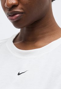 Κοντινή λήψη ενός ατόμου που φοράει λευκό μπλουζάκι Nike με το μαύρο λογότυπο Nike Swoosh ορατό στον λαιμό.