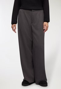 Pantaloni a gamba larga in tessuto grigio scuro, con una texture liscia, frontale piatto e tasche laterali. La vita è plissettata per una vestibilità su misura.